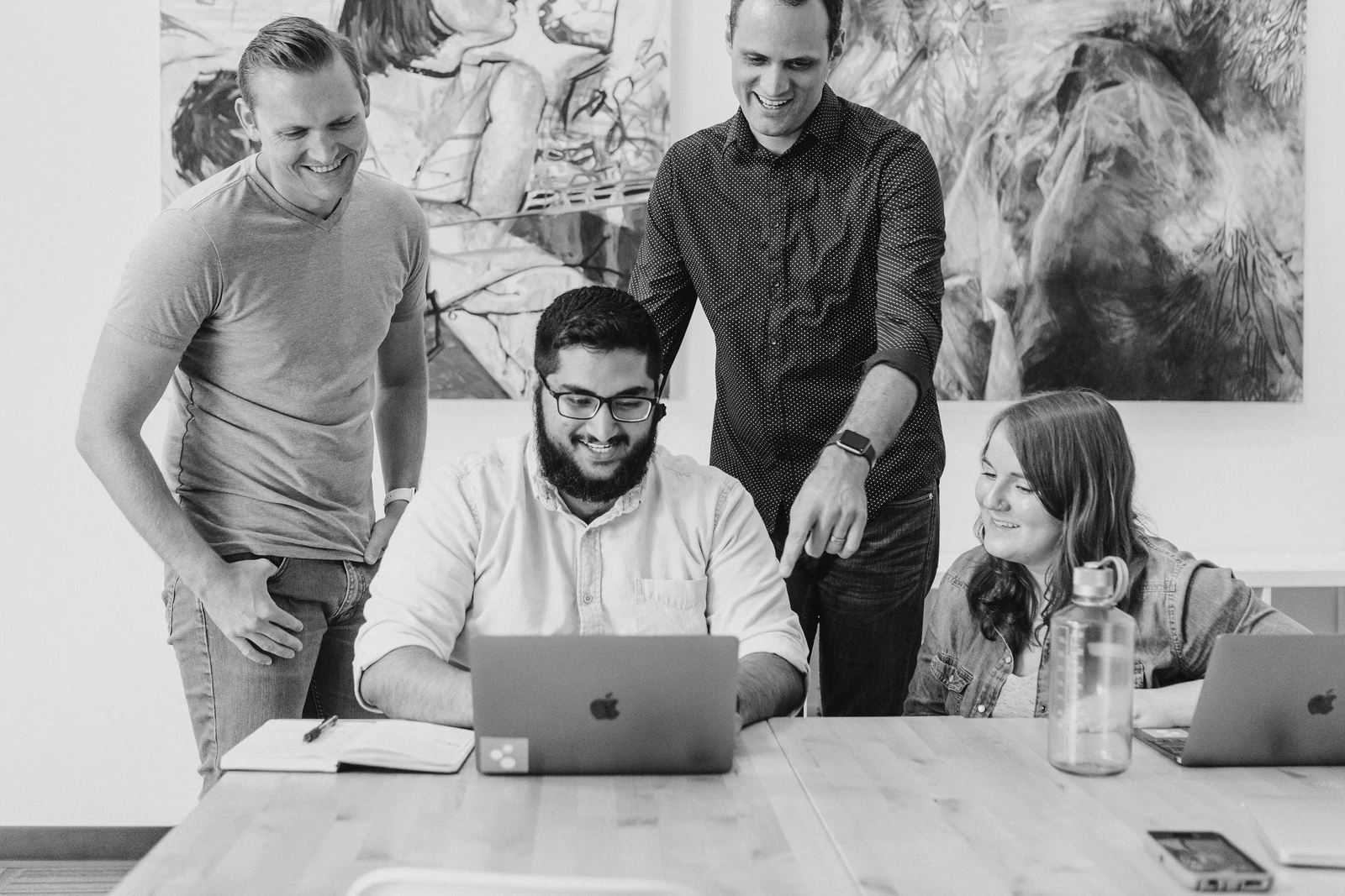 four coworkers smiling around laptop at table. Photograph accompanying Velaharra’s cultural platform guide.